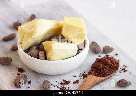 Kakaobutter oder Kakaobohnenfestes Öl und rohe Kakaobohnen auf rustikalem Hintergrund, gesundes natürliches Öl Stockfoto