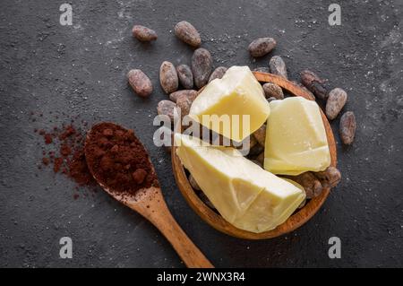 Kakaobutter oder Kakaobohnenfestes Öl und rohe Kakaobohnen auf rustikalem Hintergrund, gesundes natürliches Öl Stockfoto