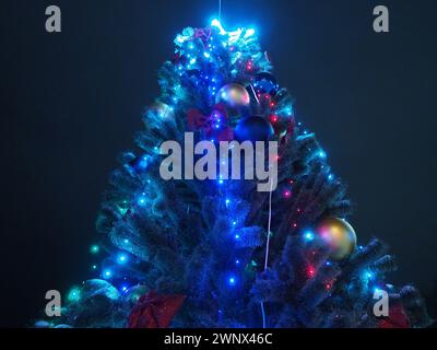 Wunderschöner Silvester- oder Weihnachtsbaum in der Stadt. Abendzeit und dunkler Himmel. Große, glänzende Kugeln und blaue Girlanden hängen am Baum Stockfoto