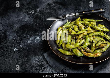 Gebratene grüne Edamame Sojabohnen mit Meersalz und Sesamsamen auf einem Teller. Schwarzer Hintergrund. Draufsicht. Kopierbereich. Stockfoto