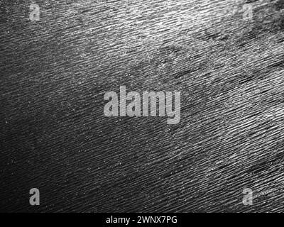 Schwarzes oder graues Wellpapier. Unebene Oberfläche. Abstrakter einfarbiger Hintergrund. Gewellte Kanten des Papierbogens. Lichtverlauf. Gewellte Textur Stockfoto