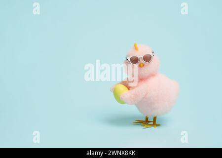 Kleine coole Küken in Sonnenbrille mit Osterei auf blauem Hintergrund, Kopierraum Stockfoto