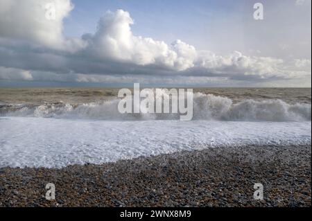 Farbe starkes Sonnenlicht von Wellen, die auf Kieselstrand Brandung, Spume & Spray brechen, grünes Meer, ein blauer Himmel mit wehenden weißen Wolken Südküste Englands Stockfoto