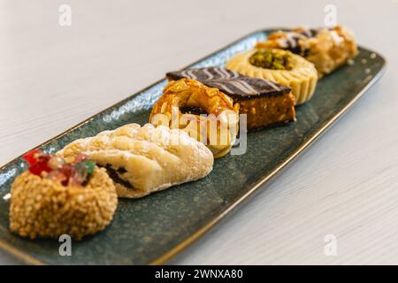 Horizontales Foto ein geschmackvolles Arrangement arabischer Gebäck-Köstlichkeiten mit verschiedenen Belägen, künstlerisch auf einer strukturierten blauen Platte serviert, ideal für h Stockfoto