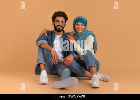 Stilvolles junges muslimisches Paar in lässigen Denim-Outfits auf beigefarbenem Hintergrund Stockfoto