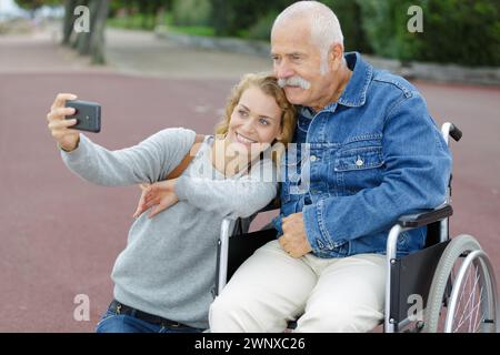 Tochter und Vater sitzen im Rollstuhl und machen Selfie Stockfoto