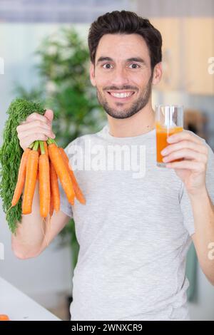 Junger bärtiger Mann trinkt frisch gepressten natürlichen Karottensaft Stockfoto