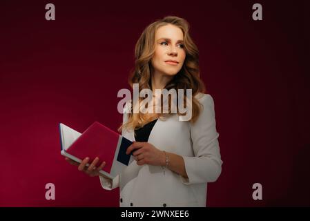 Porträt einer klugen jungen Dame, die das Kinn lernt, in einem Literaturbuch der Universität, das isoliert auf rotem Hintergrund aussieht Stockfoto