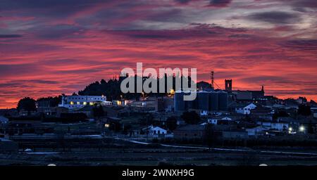 Roter Himmel über der Stadt Arbeca im Frühling mit blühenden Mandelbäumen (Les Garrigues, Lleida, Katalonien, Spanien) ESP: Cielo rojizo sobre Arbeca, Lérida Stockfoto