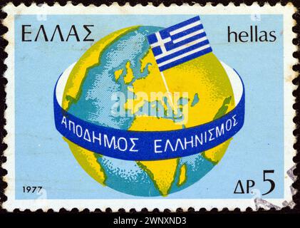 GRIECHENLAND - UM 1977: Ein in Griechenland gedruckter Stempel aus der Ausgabe "Griechen im Ausland" zeigt Globe und griechische Flagge Stockfoto