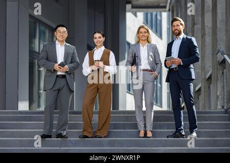 Eine Gruppe von elegant gekleideten Unternehmensexperten wird beobachtet, wie sie eine Pause von der Arbeit auf den Stufen außerhalb ihres Arbeitsplatzes machen und Teamarbeit, Erfolg und das Geschäftsleben in der Stadt verkörpern. Stockfoto