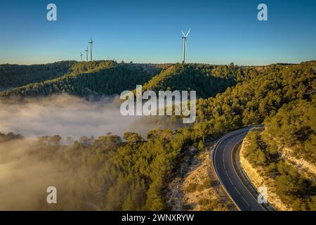 Blick aus der Vogelperspektive auf das Fatarella-Gebirge und die Windräder des Windparks über dem Nebel bei Sonnenaufgang (Tarragona, Katalonien, Spanien) Stockfoto