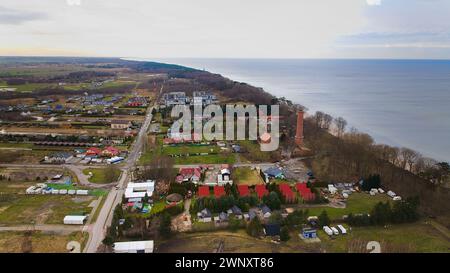 Ein Drohnenfoto zeigt den Strand von Gąski, Woiwodschaft Westpommern, Polen, mit einem Leuchtturm aus rotem Backstein, Ostsee, Sandstrand, blattlose Dünenbäume und hol Stockfoto