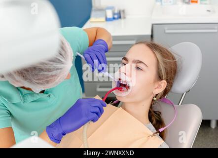 Konzept der zahnärztlichen Versorgung. Der Prozess der Montage kieferorthopädischer Keramikhalterungen. Nahaufnahme der Hände des Zahnarztes mit blauem Leim auf die Reinigung des Patienten Stockfoto