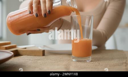 Nahaufnahme unerkennbare Frau gießt Orangensaft aus dem Glas auf den Küchentisch. Weibliche Hände gießen frisches Getränk Pfirsich Aprikose Smoothie gesund Stockfoto
