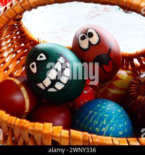 Ostereier in verschiedenen Farben mit gemalten lachenden Gesichtern. Lustige Grimaces mit Augen, Zunge und großen weißen Zähnen. Gruseliges Gesicht für Halloween Stockfoto