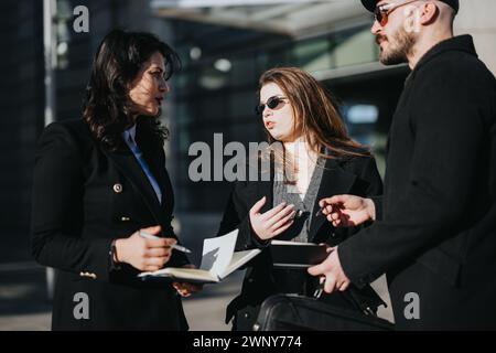 Dynamisches Bild von drei Jungunternehmern, die sich an einer Diskussion beteiligen, während sie vor einem sonnigen Stadtkulisse Gadgets und Notizen halten. Stockfoto