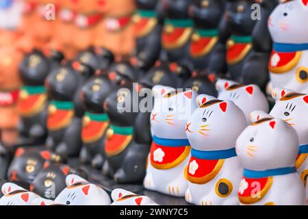 Ein Haufen ausgerichteter winziger und bezaubernder, handgemalter weißer japanischer Manekineko-Katzen mit Glücksbringer-Skulpturen, die die berühmte heranziehende Katze darstellen Stockfoto