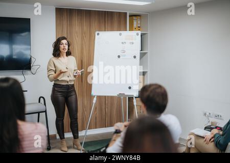 Selbstbewusste Moderatorin, die während eines Bürogesprächs Strategien mit einem Marker vor einem Whiteboard diskutiert. Stockfoto