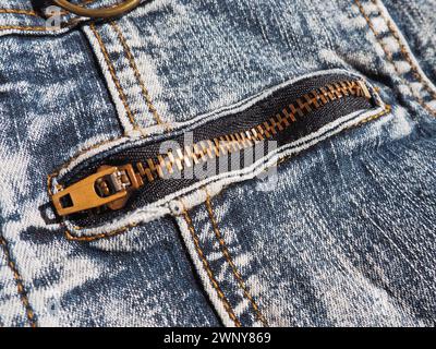 Close-up-Denim mit Nähten und Locken. Stark schäbig getragene Jeans. Gelbes Metallschloss aus Bronze mit Laufschiene. Jeans mit Tasche Stockfoto