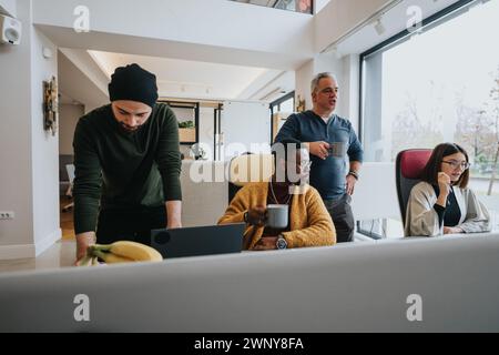 Ein multiethnisches Büroteam nimmt an einer Projektdiskussion Teil. Kollegen mit Kaffeetassen arbeiten an einem gut beleuchteten Arbeitsplatz am Computer zusammen. Stockfoto