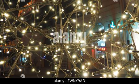 Straßengirlanden mit weißen kleinen Lampen am Abend auf einer Stadtstraße. Festliche Neujahrsdekoration Stadtstraßen und Parks Stockfoto