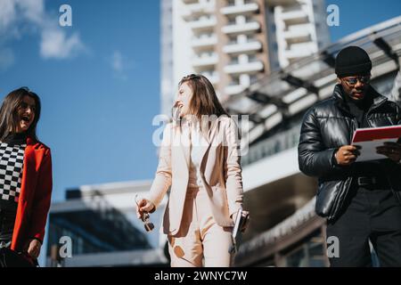 Zwei fröhliche junge Frauen werden mit Freude plaudern gesehen, während ein fokussierter Mann ein Dokument liest, im Freien in einer modernen städtischen Umgebung. Stockfoto