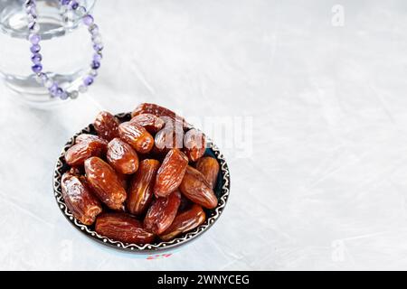 Datum Obst in Schüssel und Wasserglas mit Gebetskegeln auf grauem Beton, Ramadan Suhoor Konzept, Kopierraum Stockfoto
