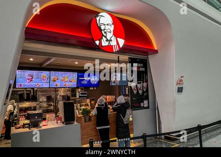 Peking, China. Dezember 2023. Passagiere betreten am 8. Dezember 2023 einen KFC-Standort im Beijing Daxing International Airport. Der Flughafen Daxing ist der größte internationale Flughafen der Welt und der zweite Flughafen in Peking. Der Flughafen wurde im September 2019 eröffnet und soll bis 2025 72 Millionen Fluggäste abfertigen. Daxing, entworfen von Zaha Hadid, wurde um einen zentralen Innenhof mit fünf Flugzeugpiers gebaut, die direkt nach außen ausstrahlen, um dem Gebäude das Aussehen eines Seesterns von oben zu verleihen. (Foto: Samuel Rigelhaupt/SIPA USA) Credit: SIPA USA/Alamy Live News Stockfoto