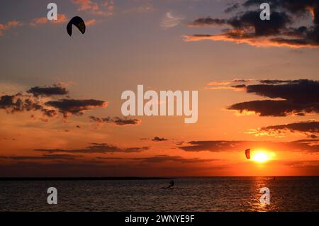 Kitesurfer gleiten weiter über das Wasser, während die Sonne in der Bucht untergeht. Stockfoto