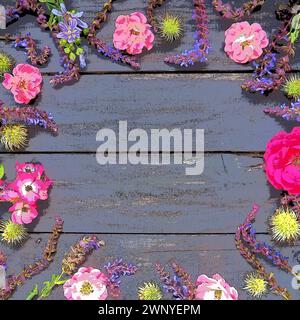 Blumen im Kreis auf hölzernem Hintergrund. Postkarte für den Urlaub. Rosen, Geranien, Lavendel, Salbei und haarige Kastanien an den Kanten im Dunkeln Stockfoto
