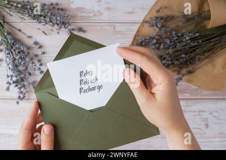 RELAX REFRESH Text zum AUFLADEN auf unterstützender Nachricht in Papierform Notizen aus grünem Umschlag. Flache Zusammensetzung trockene Lavendelblüten. Konzept von innerem Glück, Verlangsamung digitaler Detox persönliche Erfüllung. Draufsicht Stockfoto