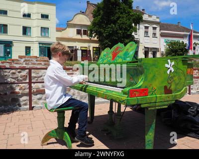 Sremska Mitrovica, Serbien, 05. Juni 2021. Ein Junge in einem weißen Hemd spielt auf der Straße Klavier. Das Kind ist 9 Jahre alt, weiß. Klavierfarben grün Stockfoto