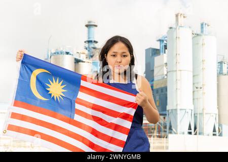 Traurige junge Frau mit der Flagge Malaysias vor dem Hintergrund der Fabrik Stockfoto