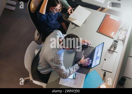 Konzentrierter Mitarbeiter, der in einer geschäftigen Arbeitsumgebung am modernen Bürotisch tätig ist. Stockfoto