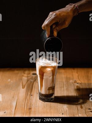 Espresso von Hand in ein Glas Milch gießen Stockfoto
