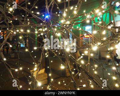 Straßengirlanden mit weißen kleinen Lampen am Abend auf einer Stadtstraße. Festliche Neujahrsdekoration Stadtstraßen und Parks Stockfoto