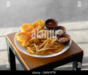 Ein Teller bestehend aus gebratenen Calamari, Pommes frites und Popcorn-Huhn, serviert mit Mayo, Ketchup und Chili-Sauce Stockfoto