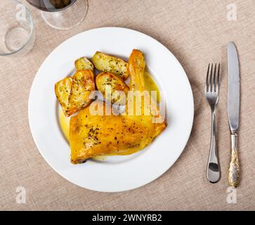 Gebratenes Hähnchen am Schenkel mit Knoblauch in eigenem Saft gewürzt und garniert mit Stücken gebackener Kartoffeln Stockfoto