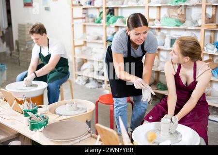 Töpferin unterrichtet junge Lehrlinge in der Werkstatt, wie man Töpferei auf Töpferrad macht Stockfoto