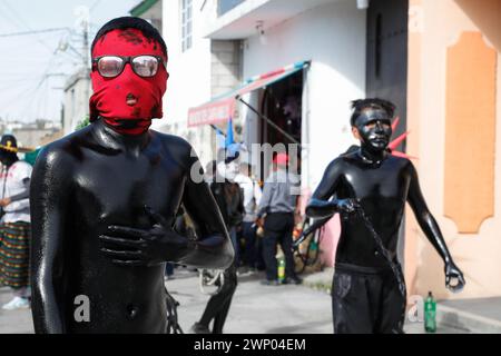 März 2024, San Nicolas de los Ranchos, Mexiko: Jugendliche mit schwarz lackiertem Körper und Masken nehmen an der vorspanischsprachigen Feier „der Karneval der Xinacates“ Teil, die in San Nicolas de los Ranchos, Gemeinde an den Hängen des Vulkans Popocatepetl, im Bundesstaat Puebla stattfindet. Als Teil der Tradition gehen die Xinacates oder gemalten Menschen auf die Straßen, um Touristen zu malen. Während dieser Feierlichkeiten wird dem Teoton-Vulkan Tribut gezollt, damit die Bewohner eine gute Erntezeit haben. Am 3. März 2024 in San Nicolas de los Ranchos, Mexiko. (Foto von es Stockfoto