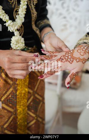Nahaufnahme des Bräutigams, der einen Ehering auf die Braut legt, die Henna auf der Hand trägt. Stockfoto