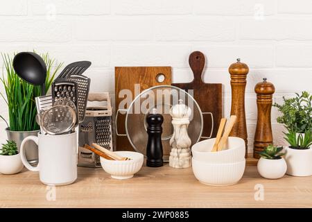 Verschiedene Küchenutensilien aus Naturmaterialien, Holz, Metall, Keramik auf einer Holzarbeitsfläche mit Topfpflanzen. Umweltfreundliche Küche Stockfoto