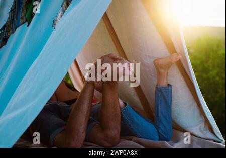 Paar auf Picknick, Camping Lifestyle mit Freundin. Rückbeine Ansicht des Paares im Zelt. Bester Freund. Konzentrieren Sie sich auf die Füße. Stockfoto