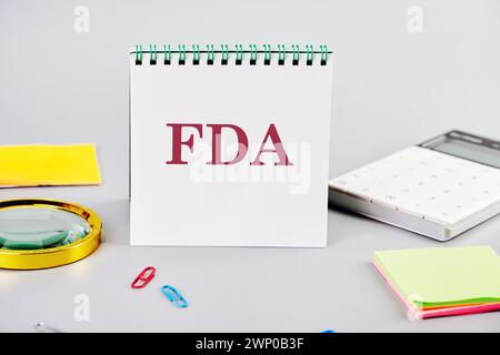 Word FDA steht auf einem leeren Notizblock neben Büromaterial auf grauem Hintergrund. Geschäftskonzept Stockfoto