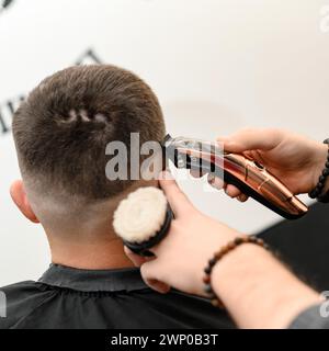 Barber rasiert die Kontur der ovalen Linie mit einem Haarschneider am Kopf des Kunden. Ein Mann mit Bart bekommt einen Haarschnitt in einem Friseurstuhl. Stockfoto