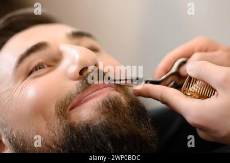 Ein Friseur-Stylist trimmt einem Kaukasier Schnurrbart mit einer Schere Stockfoto