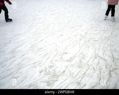 Eisdecke auf der Eislaufbahn mit Schnee und Spuren von Schlittschuhstellen. Beine von Menschen in Schlittschuhen. Kopierbereich Stockfoto