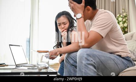 Ein unglückliches und gestresstes junges asiatisches Paar hat einen Streit über ihre Haushaltsausgaben und Finanzen und streitet über hohe Inlandsrechnungen auf einem Sofa Stockfoto