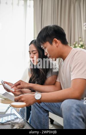 Ein nettes, junges asiatisches Paar plant ihre Ersparnisse und verwaltet ihre Haushaltsrechnungen gemeinsam im Wohnzimmer. Verheiratetes Paar und finanzieller Betrüger Stockfoto